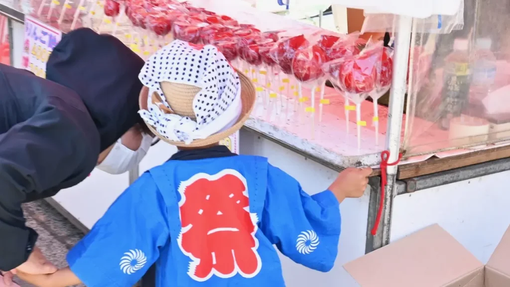 沖縄の夏祭りの屋台でりんご飴を選ぶ子ども