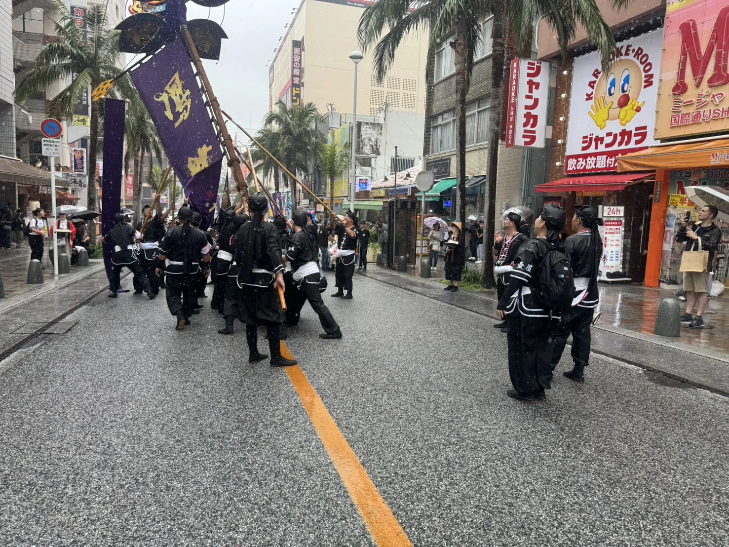 雨の国際通りで旗頭を支える参加者たち